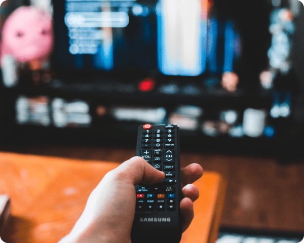 Person holding a Samsung remote control while watching TV with an on-screen menu.
